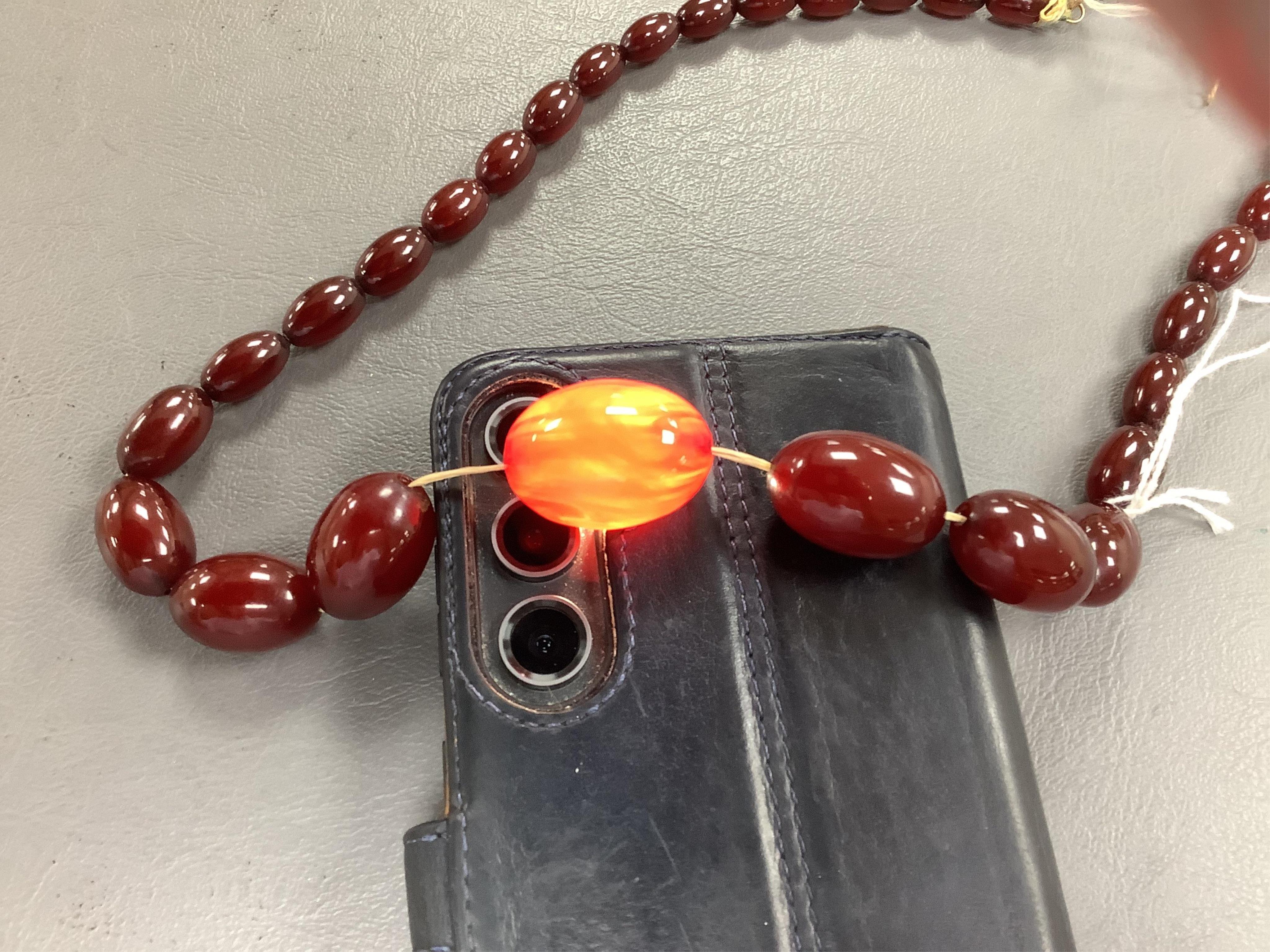 A cherry-coloured bakelite imitation amber necklace, composed of graduated oval beads measuring approximately 1.2-3cm, length 56cm, gross weight approximately 54 grams